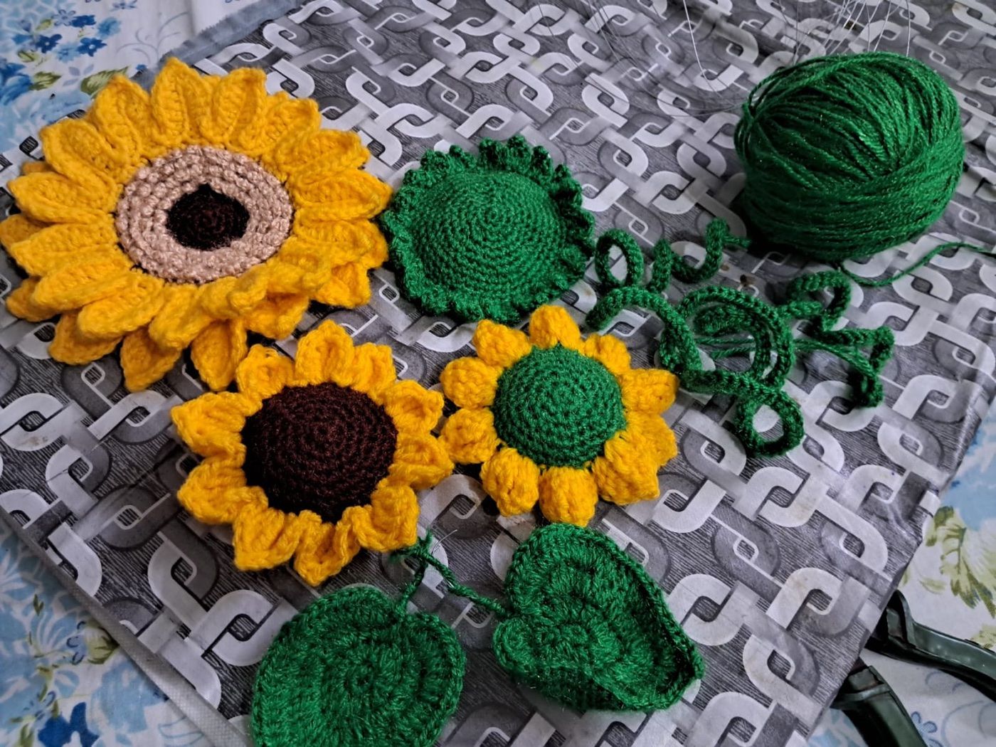 Finished and in-progress crochet sunflowers laid out with green yarn, showing how each piece comes together